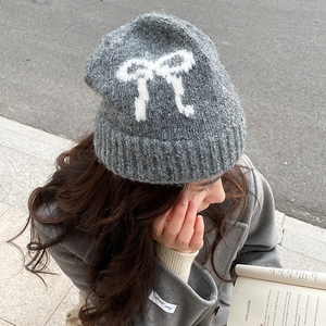 Top view of a gray knit beanie featuring a white bow pattern worn in a street setting