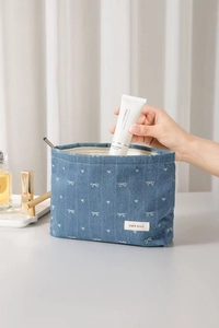 Putting hand cream into a blue denim makeup bag with white bow pattern and leather tag