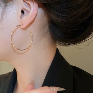 Gros plan d'une grande créole dorée minimaliste portée par une femme de profil
