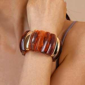 Close-up of chunky amber resin and gold metal link bracelet on a woman's wrist
