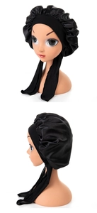 Detail of black satin baby sleep cap with long adjustable ribbons on a display head