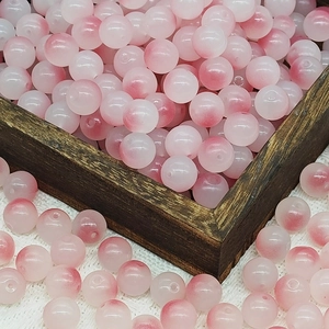 Close-up of 10mm pink and white gradient glass beads spilling from a wooden box for DIY jewelry
