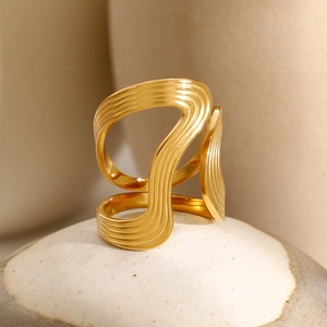 Elegant gold-tone stainless steel ring with hollow wave design on a ceramic pedestal