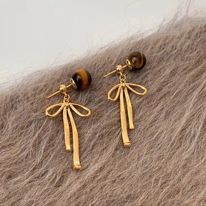 Macro view of gold bow earrings featuring natural tiger eye beads on soft plush background