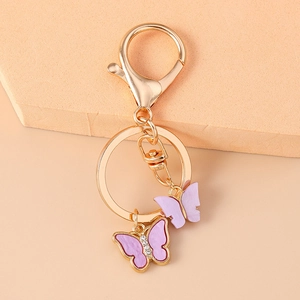 Detailed view of purple rhinestone butterfly keychain with gold lobster clasp on beige base