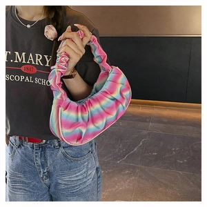 Close-up of rainbow gradient pleated cloud bag held by a model in a stylish indoor setting