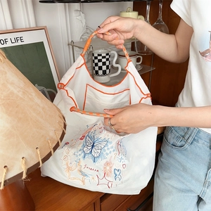 Détail du sac cabas blanc avec broderie papillon bleue et poignées en corde tressée orange