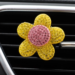 Close-up of yellow and pink crystal flower car air vent clip on black dashboard