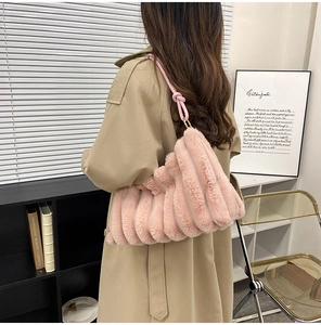 Close-up of pink plush shoulder bag with knotted strap on a model wearing a trench coat