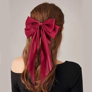 Detail view of a large burgundy satin bow hair clip on model's hair with ribbons