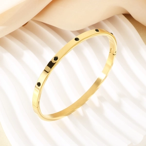 Macro detail of a gold bangle with black stones set on a white textured stand