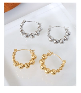 Polished silver and gold beaded hoop earrings shown on a reflective white surface