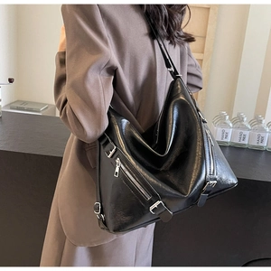 Detail of a black high-gloss faux leather crossbody bag with silver zippers and moto style