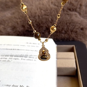 18K gold-plated tiger eye gourd necklace with crystal accents on a vintage book backdrop