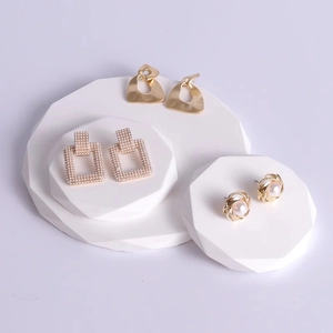 Three pairs of elegant gold and pearl earrings displayed on white geometric jewelry stands