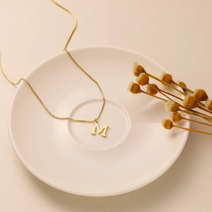 Macro detail of gold-plated box chain and capital letter M pendant in ceramic dish