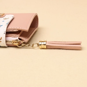 Dettaglio del portafoglio in pelle PU rosa con patta floreale, zip dorata e nappa in pelle