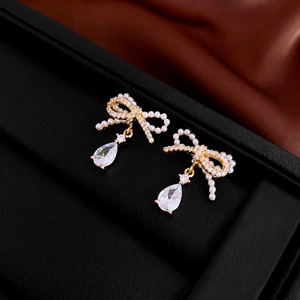 Detail of golden bow earrings with imitation pearls and teardrop zircon on black velvet