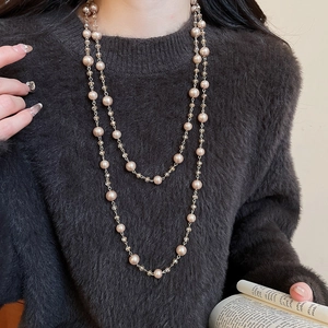 Detail of layered gold chain necklace featuring champagne pearls and clear crystals on a sweater