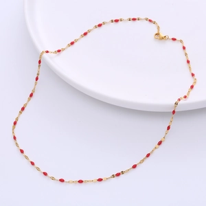 Gold titanium steel link necklace with red enamel lip charms on a white ceramic plate