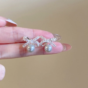 Detail of silver bow earrings with sparkling stones and dangling pearl drop charm