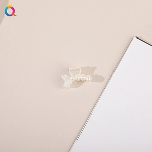Detailed view of a small mermaid tail hair clip with four faux pearls on a clean surface
