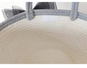 Detail of grey cotton rope handle and black mesh bow on beige woven tote bag