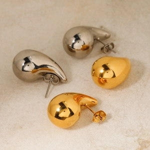 Polished gold and silver teardrop earrings displayed on a minimalist marble surface