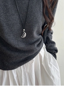 Detail of silver comb-shaped pendant on long black cord necklace with grey sweater