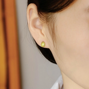 Macro shot of 14k gold pear-cut green olive stone stud earring worn on model ear