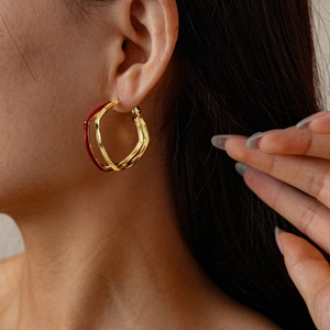 Primo piano di orecchini a onde placcati oro 18k con smalto rosso indossati da modella