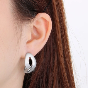 Close-up of a silver-toned abstract twisted geometric hoop earring on a model ear