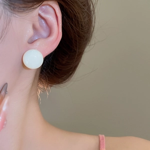 Close-up of minimalist cream white button stud earring worn by a model on the earlobe