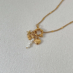 Detail of gold necklace with starfish, cherry, heart charms and irregular pearl pendants