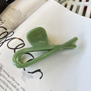 Close-up of a pale green claw clip with smooth resin finish on an open magazine page