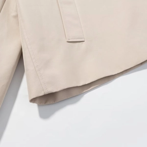 Detailed macro view of the beige twill fabric texture and clean hem stitching on the jacket