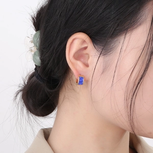 Close-up of gold stainless steel hoop earrings with blue textured inlay on model