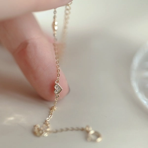 Close-up of a gold heart charm bracelet with sparkling diamonds on a delicate O-chain