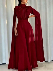 Deep red pleated jumpsuit featuring dramatic floor-length cape sleeves and high neck detail