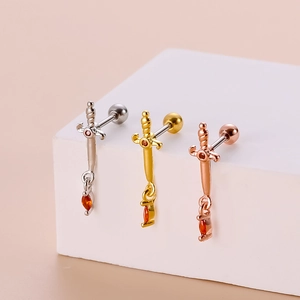 Three sword-shaped stud earrings in silver, gold, and rose gold with red gemstones