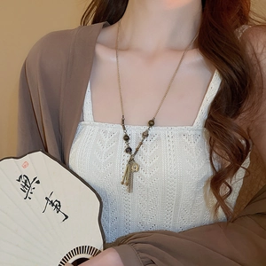 Dettaglio di una collana vintage di perline con monete e nappe indossata con ventaglio