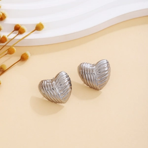 Close-up of silver heart-shaped earrings with textured finish on a decorative wave stand