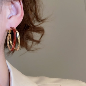 Close-up of model wearing geometric gold and burgundy petal-shaped statement earrings