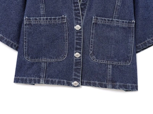 Détail d'un haut en jean bleu foncé avec poches plaquées et boutons métalliques