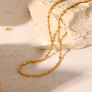 Dettaglio della collana a catena con grani ovali placcata oro 18K su pietre beige