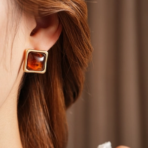 Close-up of a square amber resin earring with a gold frame worn on a model's ear