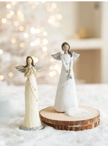 Close-up of resin angel figurines with silver glitter wings on a snowy wood base