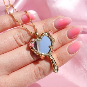Gold heart-shaped mirror pendant necklace with floral details on pink silk background