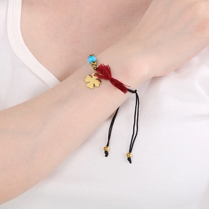 Detail of woven bracelet with gold clover charm, blue bead and red tassel on wrist