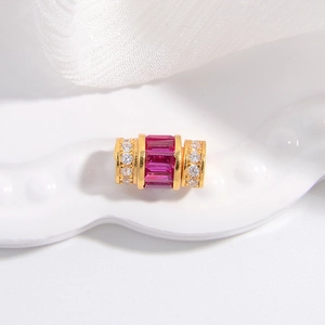Détail macro d'un charm cylindrique doré serti de cristaux rouges et de zircons